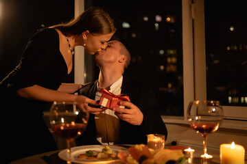 A woman gives a man a gift box on Valentine's Day, a passionate kiss of a couple at dinner on a...