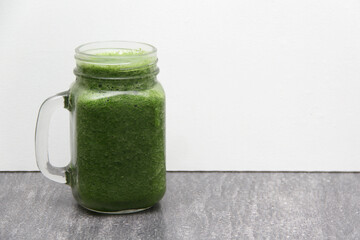 Green juice made from vegetables such as cucumber, lemon, spinach, chard, celery served in a glass mason jar for a healthy, vegan and nutritious breakfast
