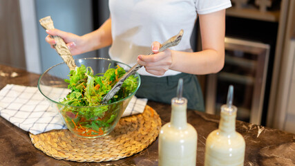 salad concept the woman with white t-shirt and dark green pants standing at the kitchen and making a bowl of green salad