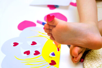 Child playing with adhesive tape paper , making funny card with sun and hearts