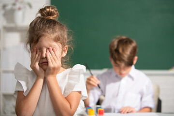 A smart school girl cry. Schoolgirl in uniform covering her face with her arm crying sad of bullying at school standing in front of blackboard. Childhood and education problem concept.