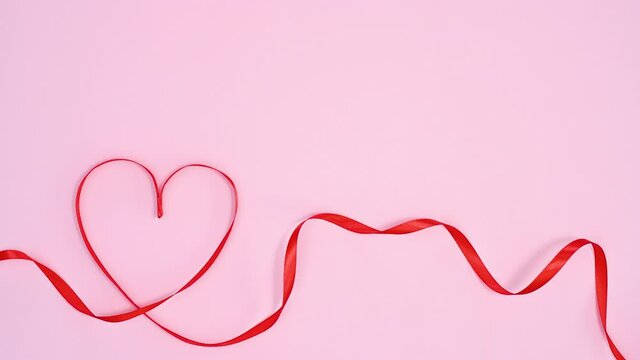 Red ribbon make Valentine's day heart on pastel pink theme. Stop motion
