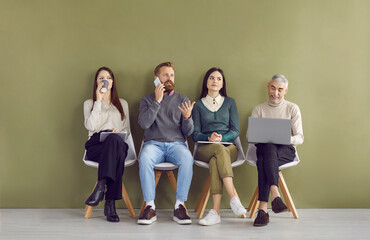 Fototapeta premium Group of different people waiting in line for business meeting or job interview, sitting on chairs by green wall in company hall or bank corridor, drinking coffee, using laptop or talking on phone