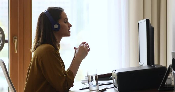 Virtual conference. Confident young female interpreter in headset work from home office by pc translate internet event online. Female expert talk before computer screen consult customer by video call