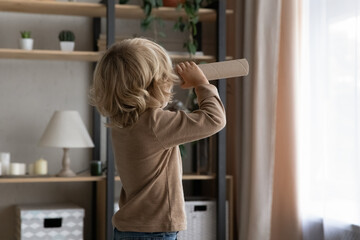Little preschool adorable boy holding toy cardboard spyglass, looking forward at window at home....