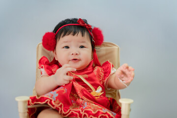 Asian chinese baby in Chinese dress sitting in white living room. Cute Asian infant baby sitting in a white living room as concept of Chinese New Year.