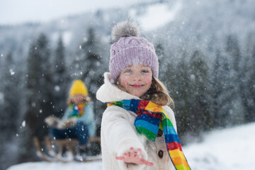 Fototapeta na wymiar Funny excited child girl face in snow on winter outdoor. Children in winter outdoor in frost snowy day. Amazed kid snowball fight in park with winter background. Expressive kids emotions.