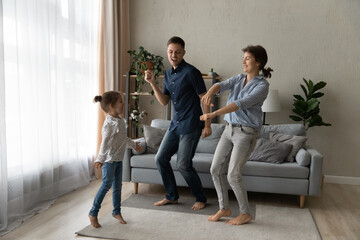Excited happy couple of parents teaching cheerful daughter girl to dance in living room. Mom, dad...