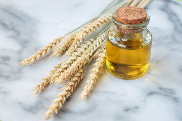 Oil in glass jar and spikelets of wheat on a light marble background. Wheat germ oil