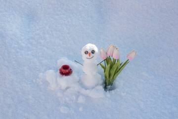 Snow man with cup coffee and spring flowers tulips. Happy smiling snowman on sunny winter day.