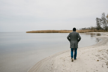 Active person in overcoat taking a walk on a winter beach