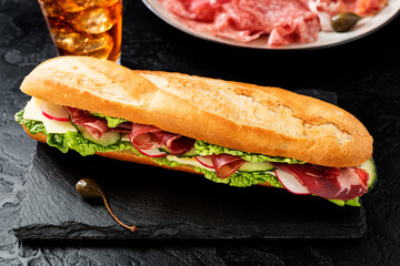 Fresh baguette sandwich with ham , cheese, cucumber and salad. Black background