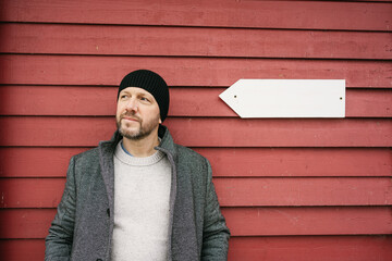 Serious man standing deep in thought in front of red timber wall