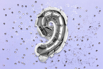 Silver foil balloon number, digit nine on a lilac background with sequins. Birthday greeting card with inscription 9. Top view. Numerical digit. Celebration event, template.