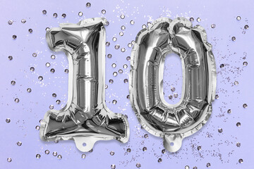 Silver foil balloon number, digit ten on a lilac background with sequins. Birthday greeting card...