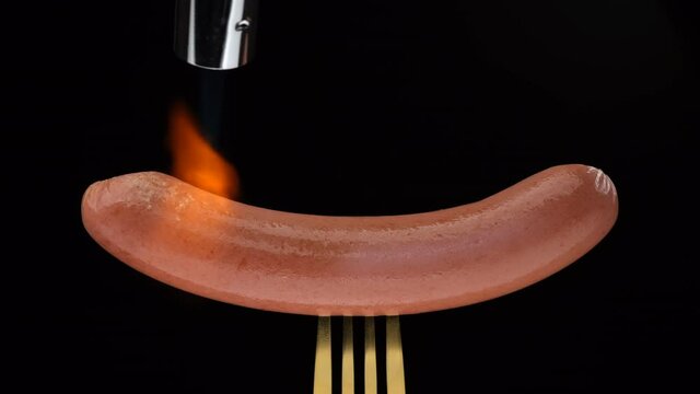 Cooking sausage using gas burner torch. Grilling sausages on black background. 4K UHD video