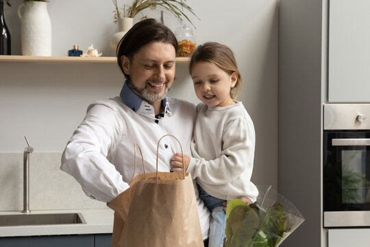 Happy Young Father Holding On Hands Adorable Little Child Daughter, Unpacking Products For Week From Carton Packet In Kitchen After Shopping In Grocery Store Or Supermarket, Healthy Dieting Concept.