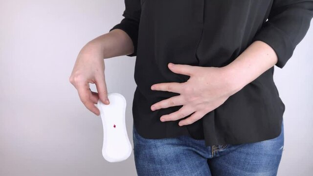 Hypomenorrhea. The woman shows a gynecological pad with a small drop of blood on it. Concept of small amounts during scanty menstruation. Complaints of pain and strange cycle. Diseases in gynecology