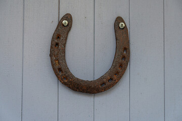 An old worn-out and rusty metal horseshoe nailed to the light lilac wooden door of a village house....