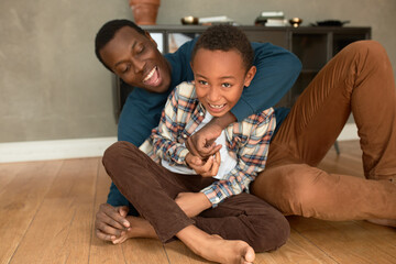 Father and son relationships. African ethnicity dad tickling and teasing his charismatic barefooted...