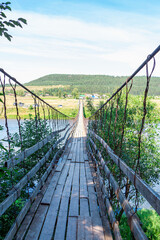 Woman with dog walks along old wooden hanging bridge on river in summer sunny day. Natural landscape. Dog on bridge