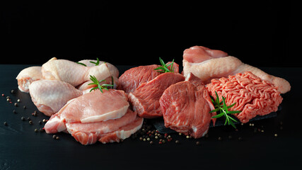 Various types of fresh meat: pork, beef, turkey and chicken on a black table.