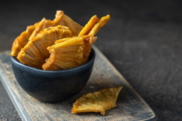 Natural dried pineapple slices in black bowl on dark background. Real fruit snack  for a health...