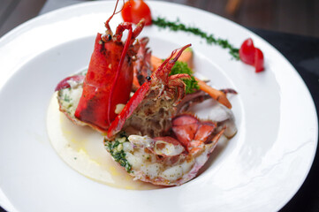 steamed american lobster with basil pesto and cherry tomato on round white plate top view
