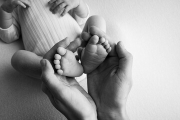 The palms of the father, the mother are holding the foot of the newborn baby. Feet of the newborn on the palms of the parents. Studio photography of a child's toes, heels and feet. Black and white.