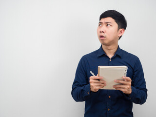 Asian man holding pen and diary feeling shocked looking at copy space