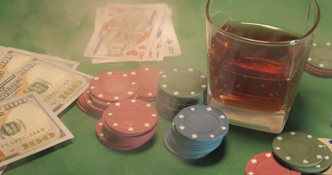 Chips, cards, a glass of whiskey and money are on the green gaming table