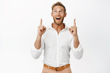 Portrait of happy businessman pointing and looking up with pleased smile, checking out big...