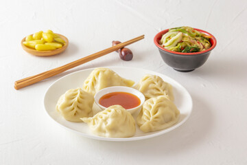 Boiled dumplings, manti or wontons with minced meat in a plate with sauce on a white table along with chopsticks, pickled mushrooms and hot peppers. Homemade food