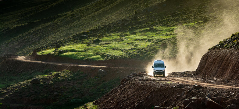 In the Atlas Mountains in Morocco. A 4x4 van lifts a cloud of dust on the dirt road that climbs towards the Tizi N’Tighist in the Ait Boulli valley