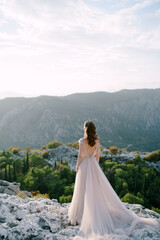 Fototapeta na wymiar Bride stands on a rocky mountain and looks out over the bay