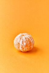  Single peeled tangerine over yellow background