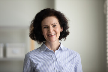 Happy confident mature businesswoman indoor head shot. Elder professional teacher, coach, boss looking at camera with toothy smile. Female business leader portrait. Leadership concept