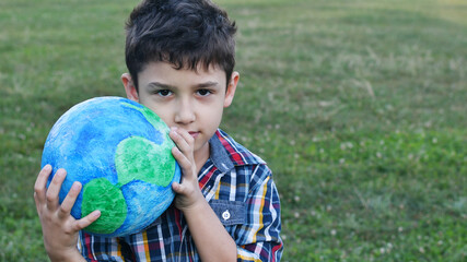 a little boy holds a globe in his hand in a meadow