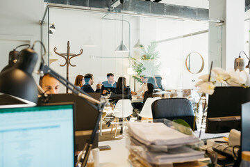 Business colleagues sitting at conference table, seen through glass wall, discussing and planning strategies, in board room at office.