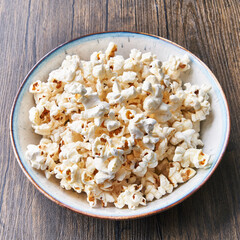  Bowl of salty popcorns on a wooden surface