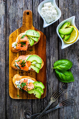 Tasty sandwiches - toasted bread with cream cheese, smoked salmon, avocado and parsley on wooden table
