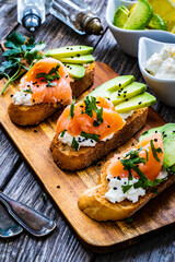 Tasty sandwiches - toasted bread with cream cheese, smoked salmon, avocado and parsley on wooden...