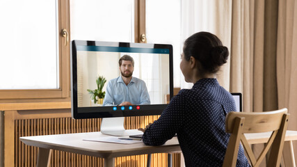 Indian millennial remote employee holding video call, talking to colleague, coach, teacher, working at home office workplace with workstation monitor, display, meeting on boss, negotiating to partner - obrazy, fototapety, plakaty