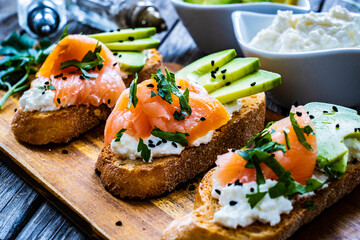 Tasty sandwiches - toasted bread with cream cheese, smoked salmon, avocado and parsley on wooden table
