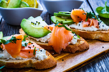 Tasty sandwiches - toasted bread with cream cheese, smoked salmon, avocado and parsley on wooden table
