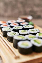 Deurstickers  Wooden board with avocado, salmon and cucumber sushi makis on a wooden surface © Krakenimages.com
