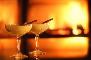 Two glasses with eggnog and cinnamon on the
 fireplace background. Background with text space.