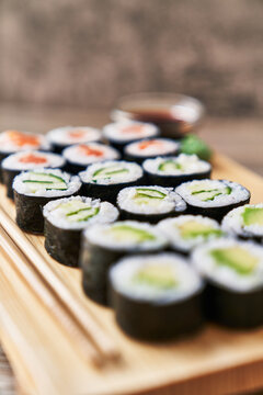  Wooden board with avocado, salmon and cucumber sushi makis on a wooden surface