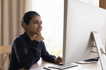 Happy successful Indian female business leader working at desktop monitor, sitting at office table,...