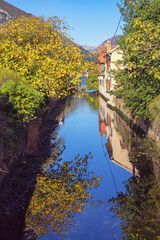 Fototapeta premium Reflection. Sky, autumn trees and building are reflected in water of canal. Kotor city, Montenegro